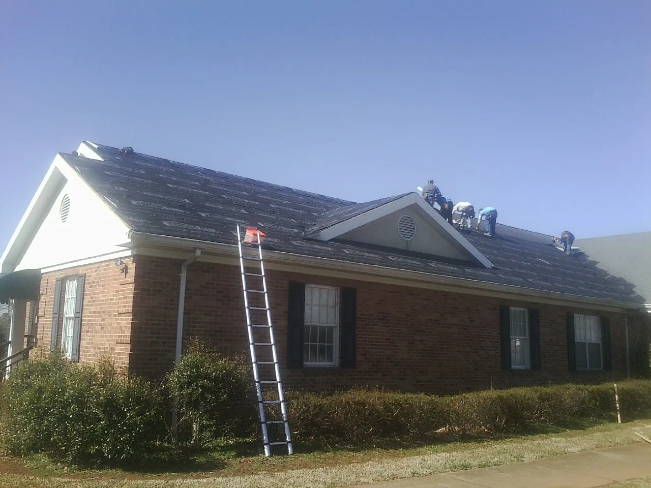 Crew tearing shingles off a brick ranch roof with a ladder set — Emergency Roof Repair work by our crew in Mill Creek