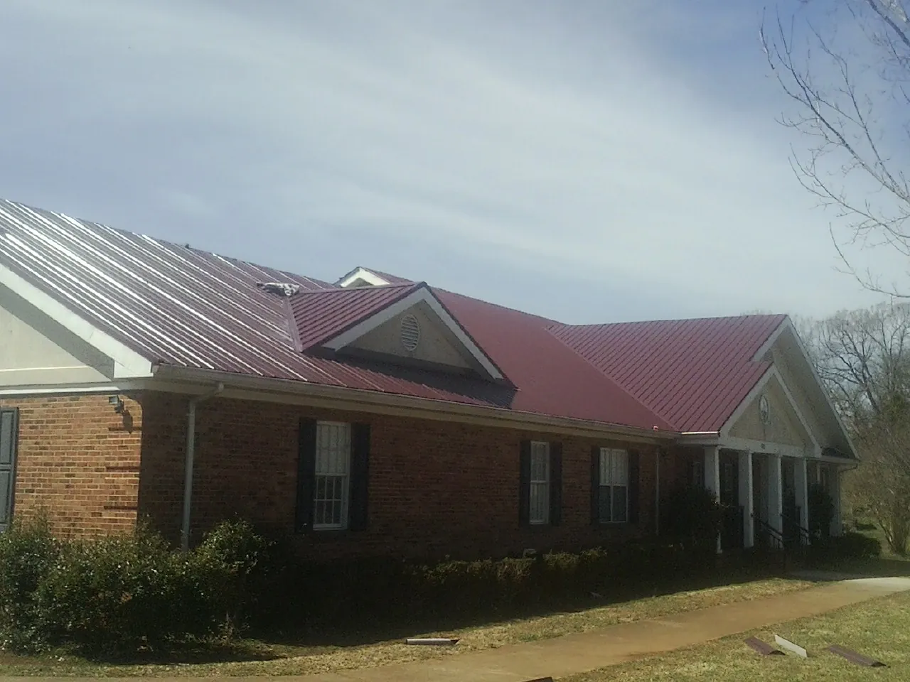 Red metal roof with gabled entries on a long brick building, from a Hail Damage Roof Repair job in Mill Creek