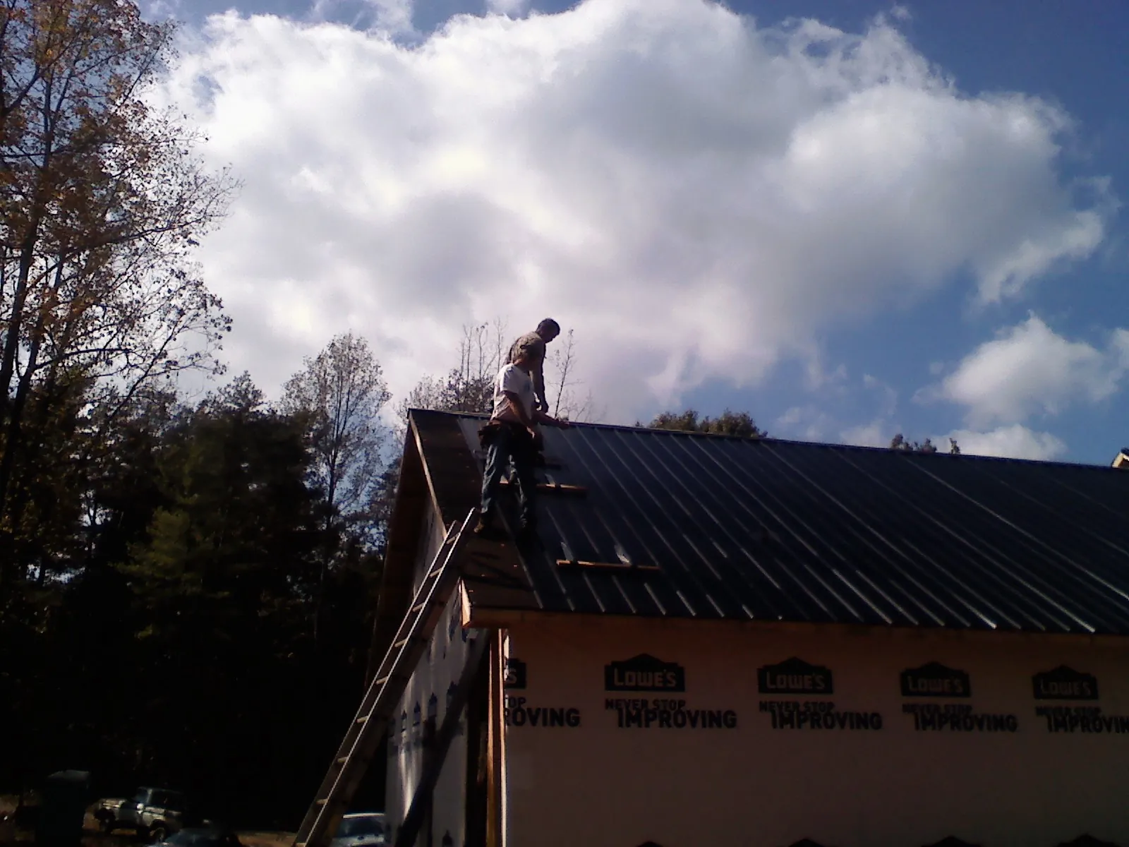 Roofer fastening dark metal panels high against a cloudy sky, from a Roof Inspection job in Mill Creek